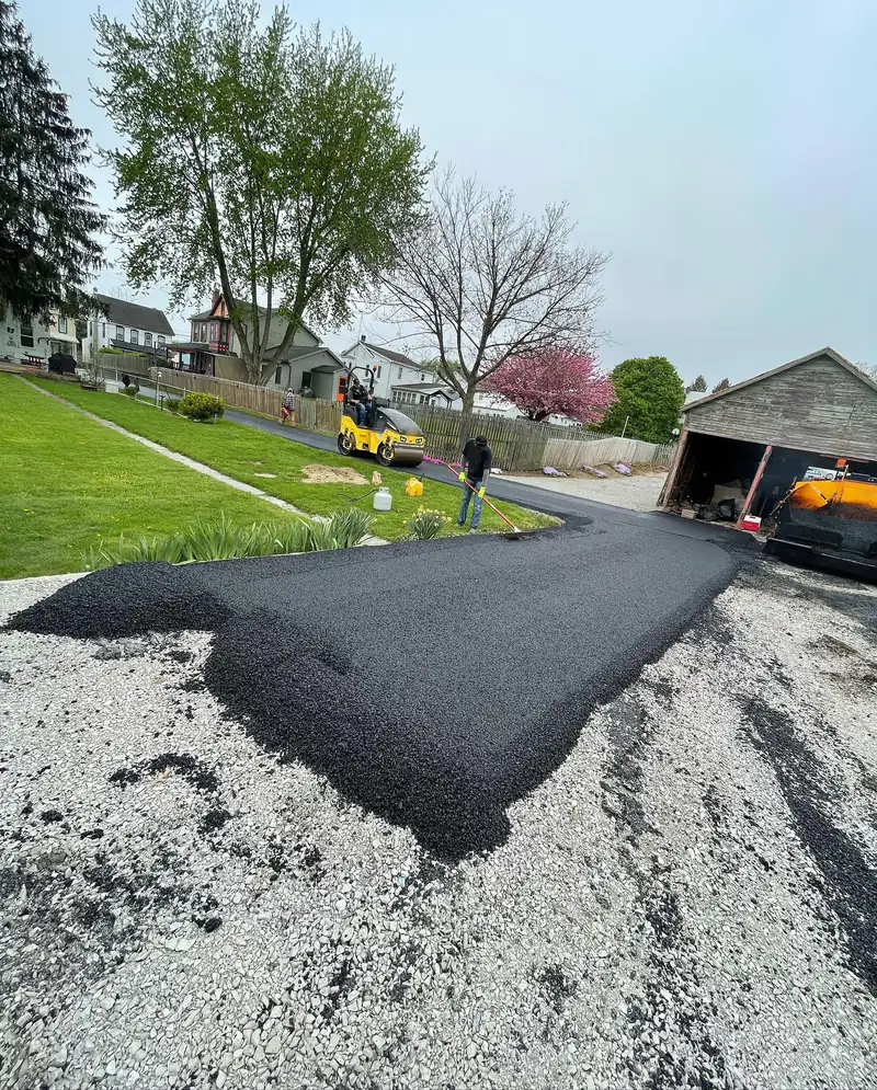 Fresh hot-mix asphalt spread over a compacted crushed stone base as a crew rakes and rolls a new residential driveway