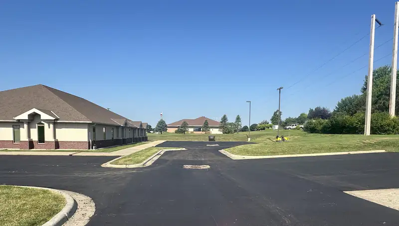 Freshly paved asphalt parking lot and drive aisle at an office park with concrete curbs and safety cones