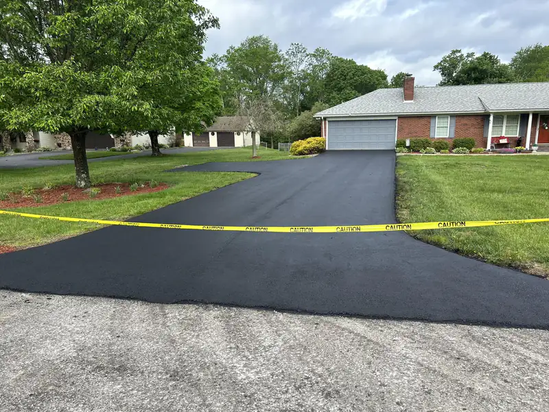 Freshly paved black asphalt driveway with a side parking extension leading to a brick ranch home's two-car garage