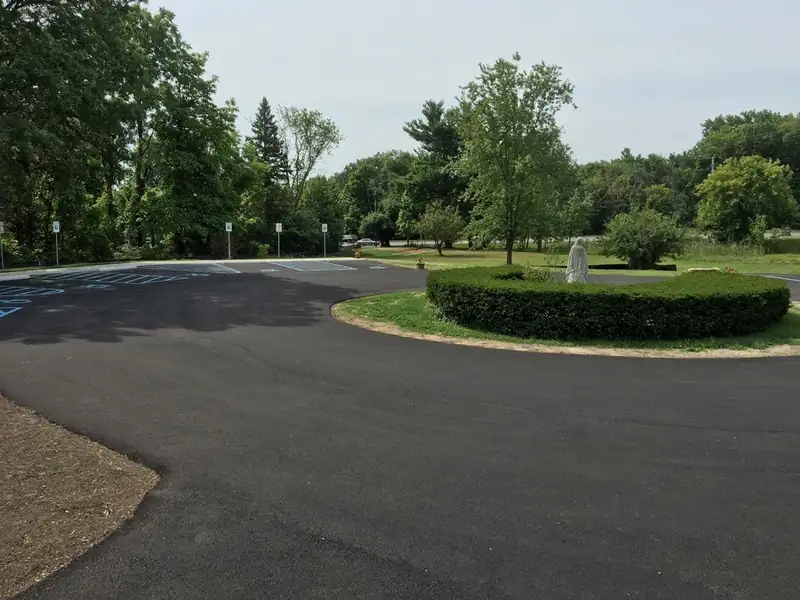 Freshly paved parking lot and circular drive with blue accessible stall striping and mature shade trees