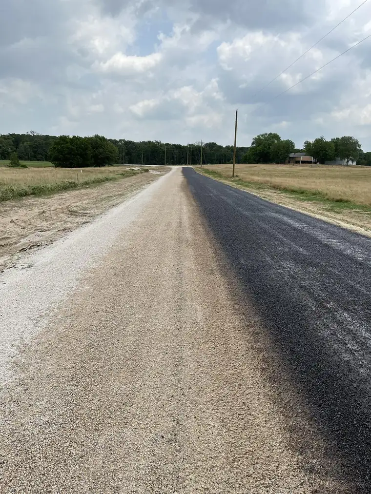 Rural road being resurfaced, with one lane of fresh dark asphalt beside a lane of light aggregate